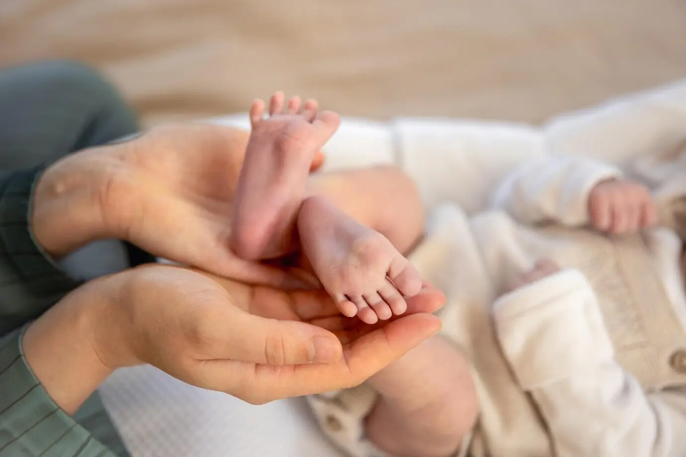 Ein Elternteil hält die Füße eines Neugeborenen in den Händen, die Mutter hält Babyfüße.